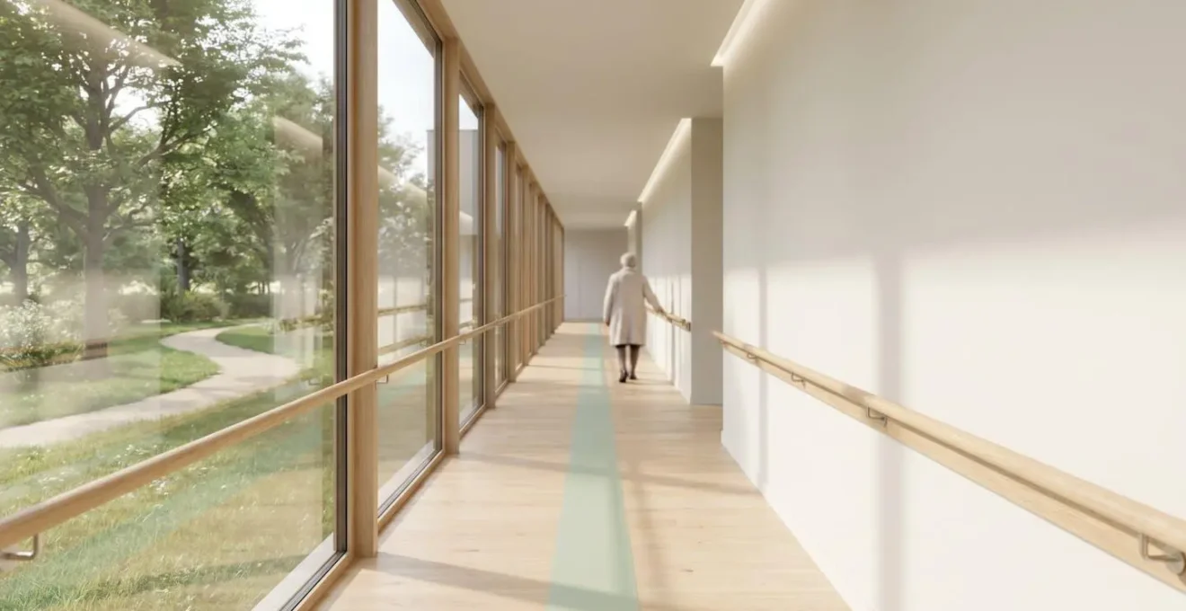 Couloir lumineux d'EHPAD avec mains courantes en bois, grandes baies vitrées donnant sur un jardin thérapeutique et marquage au sol discret.